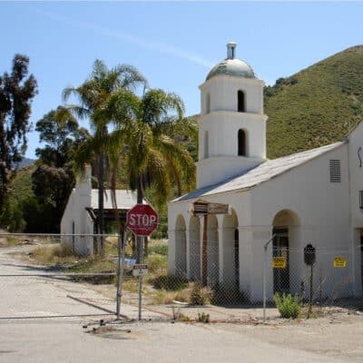 The historic first motel in San Luis Obispo, featuring a white building with a tower, palm trees, and a stop sign behind a fence