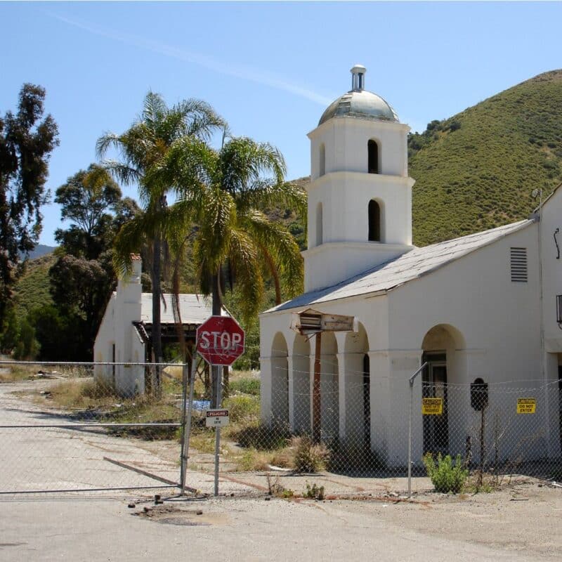The historic first motel in San Luis Obispo, featuring a white building with a tower, palm trees, and a stop sign behind a fence