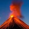 A volcano erupting with bright lava and smoke against a clear blue sky