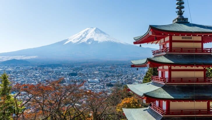 Snow-capped Mt Fuji in the background with a traditional multi-tiered Japanese pagoda in the foreground overlooking a cityscape