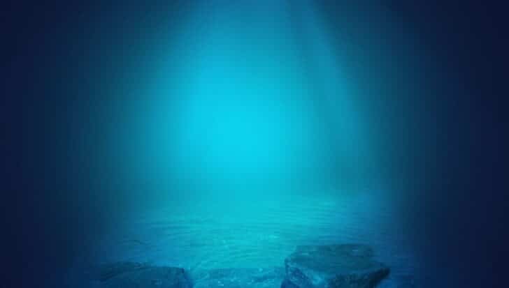 Underwater view with rocks on the seabed and blue water illuminated by light.