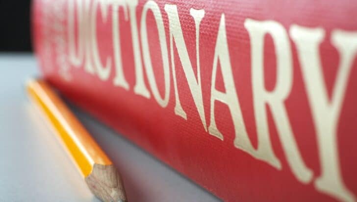 Close-up view of a red dictionary with gold lettering and a yellow pencil lying beside it