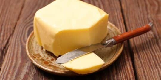Block of butter on a rustic plate with a knife on a wooden surface