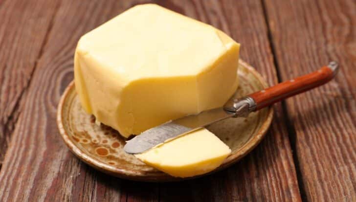 Block of butter on a rustic plate with a knife on a wooden surface