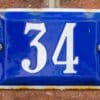 Blue enamel sign with the number 34 mounted on a brick wall