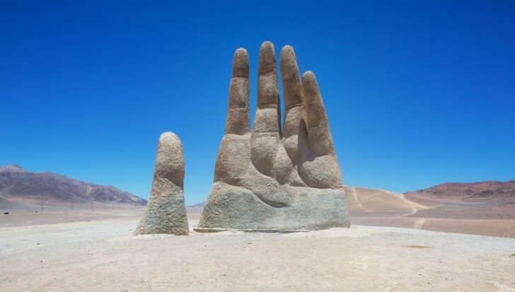 The Hand of the Desert sculpture rises from the arid landscape under a clear blue sky