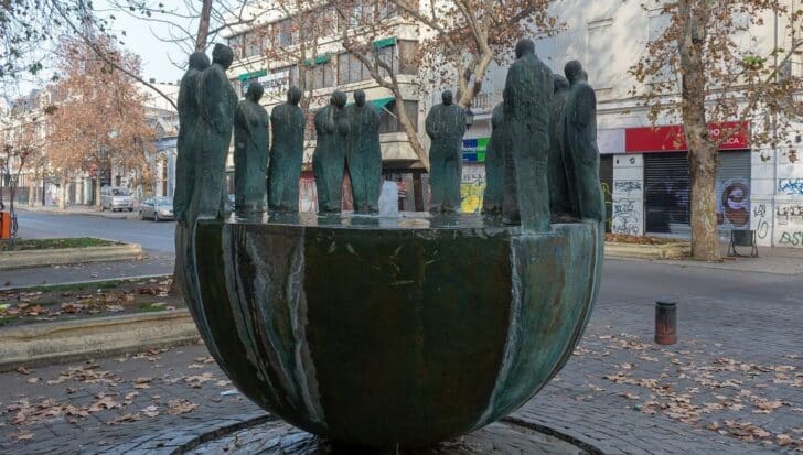 Sculpture by Mario Irarrázabalin an urban setting with multiple figures standing on a large, round base