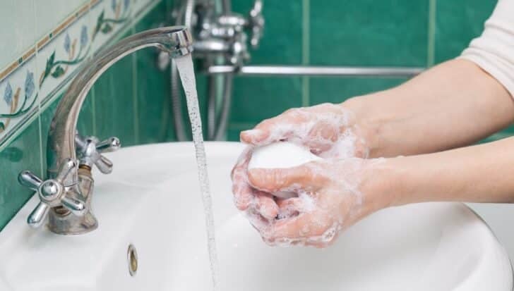 Person washing hands with a bar of soap under a running faucet