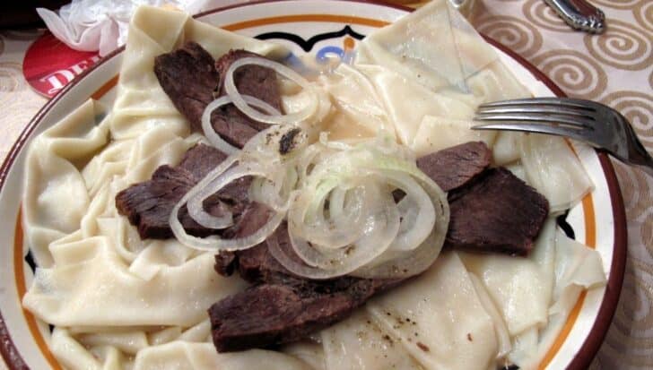 Plate of Beshbarmak, the national dish of Kyrgyzstan, featuring sliced meat, onions, and flat noodles