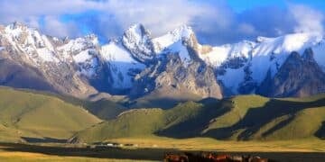 Snow-capped mountains in Kyrgyzstan with a grassy valley and a group of horses in the foreground