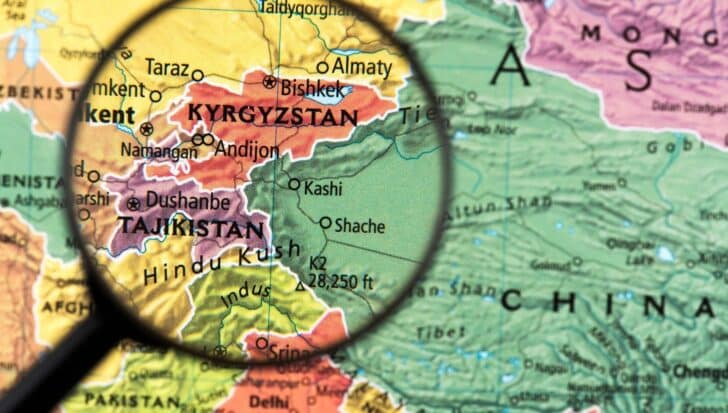 Magnifying glass highlighting Kyrgyzstan on a map, showing its position as a landlocked country surrounded by Kazakhstan, Tajikistan, Uzbekistan, and China