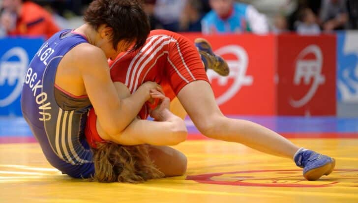 Two wrestlers in competition, one wearing a blue singlet and the other in red, engaged on a mat during a match