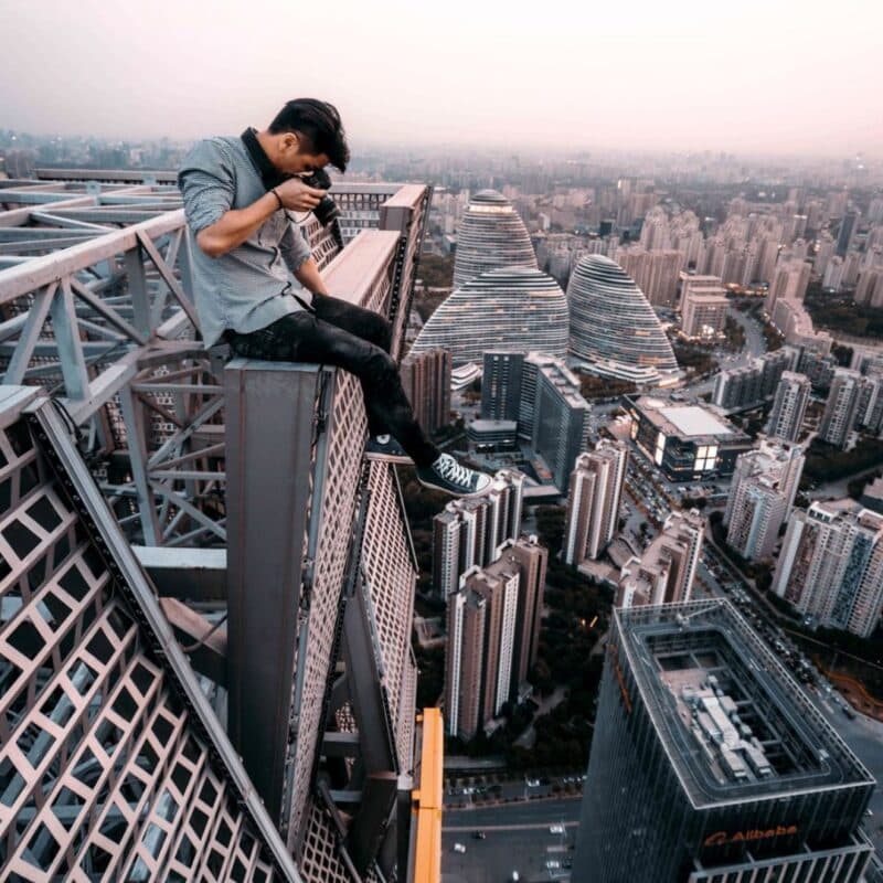 A person sitting on the edge of a tall structure, holding a camera