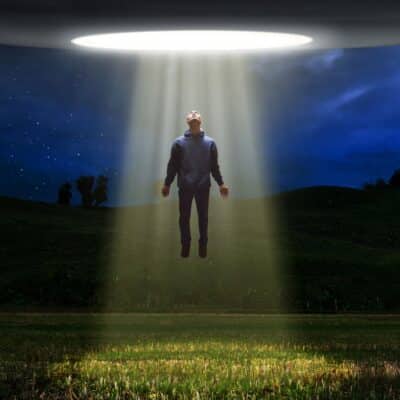 A person levitating towards a bright beam of light projected from a UFO
