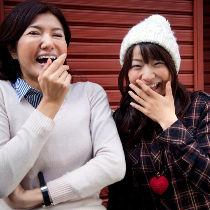 Two women laughing while covering their mouths with their hands