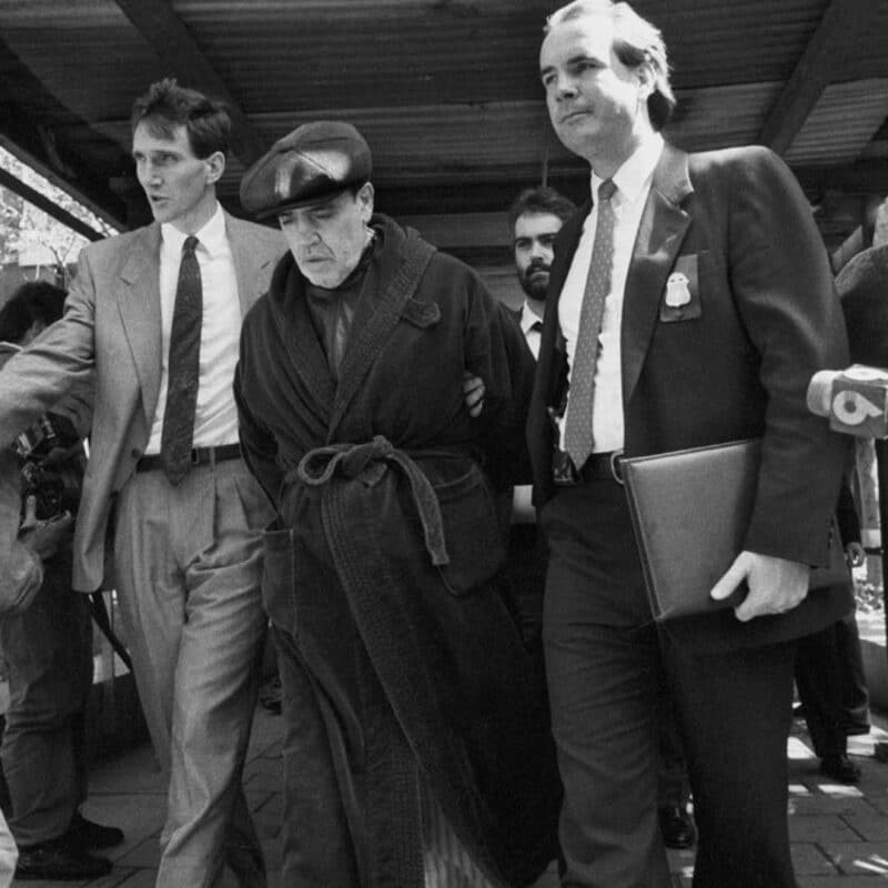 Vincent Gigante, wearing a bathrobe and cap, being escorted by two men
