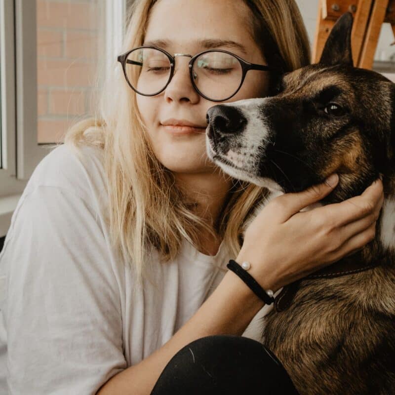 A person with glasses affectionately holding a dog close to their face