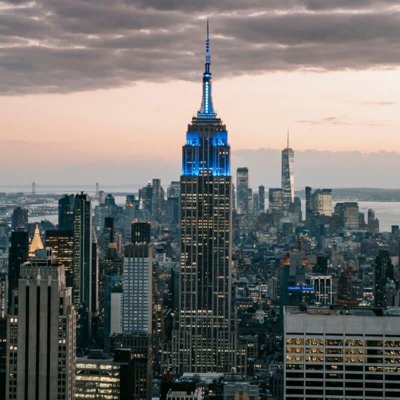Empire State Building illuminated in blue lights, towering over the New York City skyline at twilight