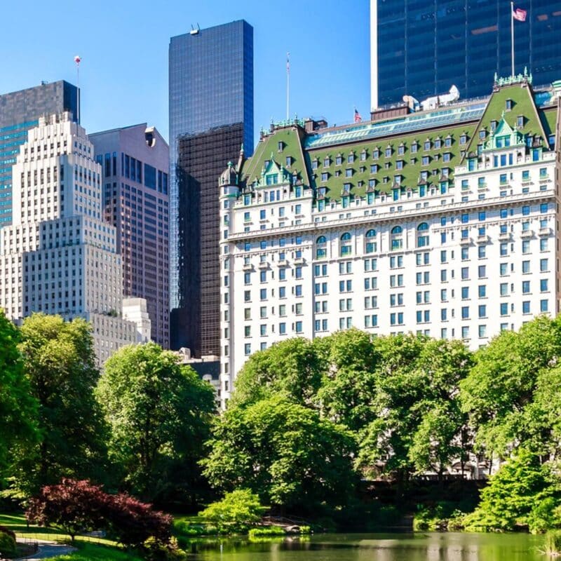 The Plaza Hotel in NYC, with its iconic green-roofed building, surrounded by trees and skyscrapers