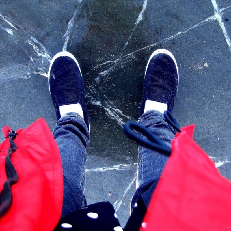 Person standing on a cracked ice surface wearing black slip-on shoes, denim jeans, and a red jacket