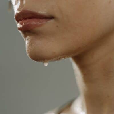Close-up of a person's face and neck sweating, with beads of sweat dripping from their chin