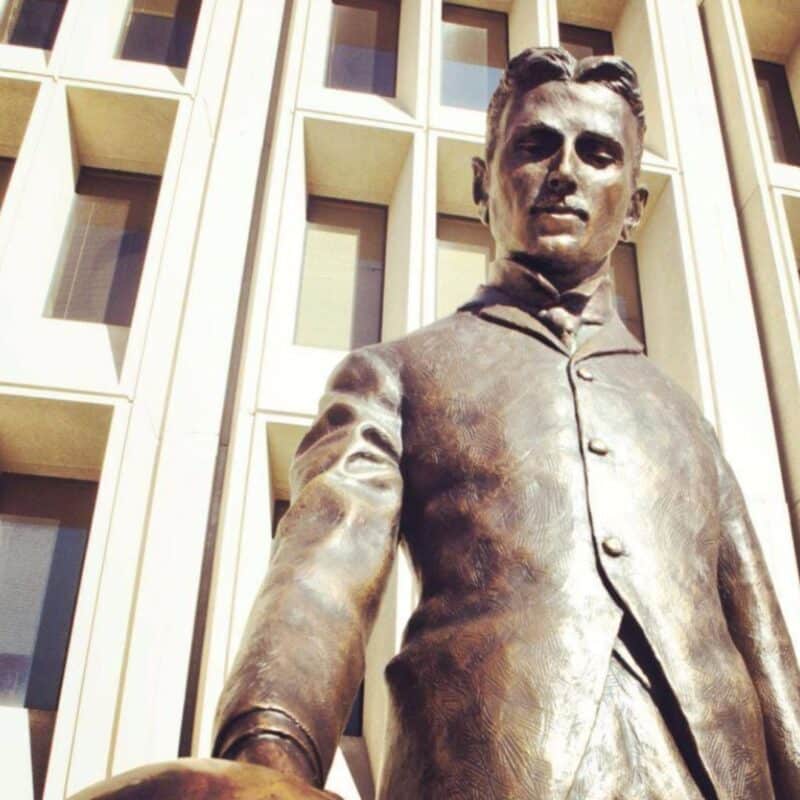Bronze statue of Nikola Tesla in front of a building with rectangular windows