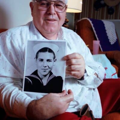 Calvin Graham holding a black-and-white photograph of himself as a young boy in a U.S. Navy uniform