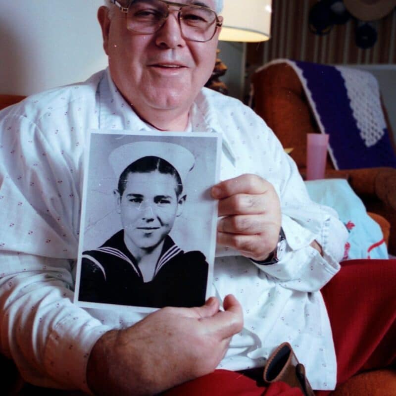 Calvin Graham holding a black-and-white photograph of himself as a young boy in a U.S. Navy uniform