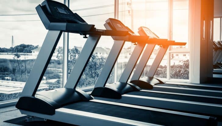 A row of treadmills positioned indoors near large windows with an outdoor view