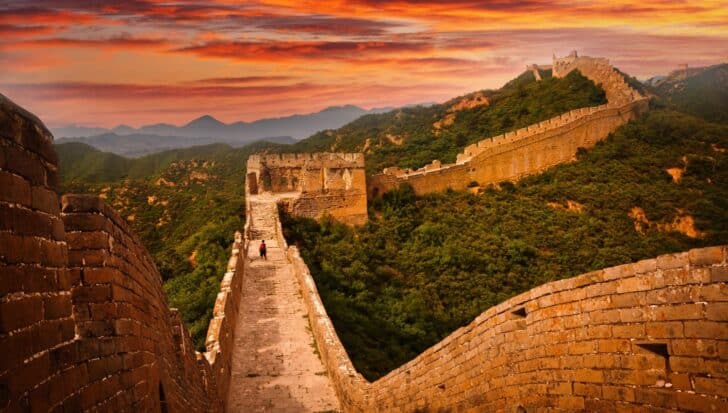 View of the Great Wall of China stretching across hilly landscape at sunset, with a person walking along the wall