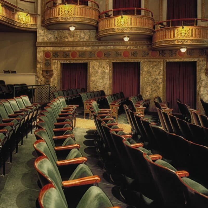 Ornate interior of a vintage movie theater with red curtains, green velvet seats, and decorative balconies