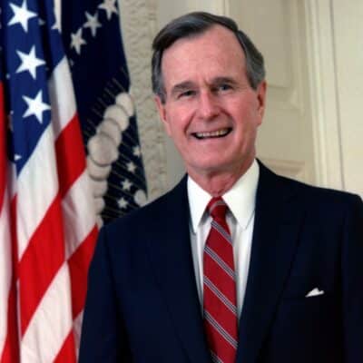 George H.W. Bush smiling, standing in front of an American flag