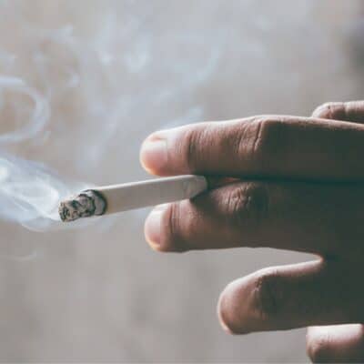 Hand holding a burning cigarette, with wisps of smoke rising
