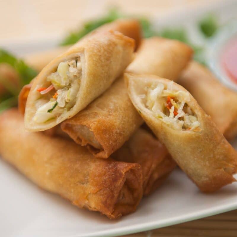 Golden-brown egg rolls stacked on a plate, showing a filling of vegetables