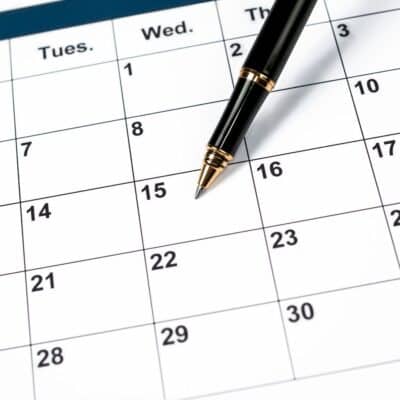 A close-up of a calendar page showing numbered dates with a black and gold pen resting on the 15th