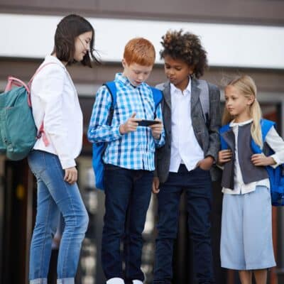 A group of four school children with backpacks, one holding and looking at a smartphone