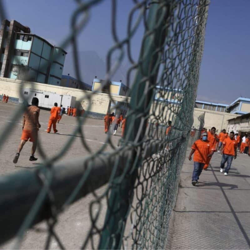 Prisoners in orange uniforms walking and standing in an outdoor area surrounded by fencing in a Mexican prison