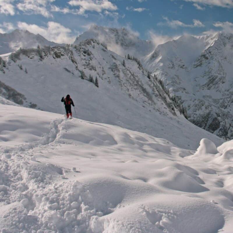 A hiker walking through a snowy, high-altitude mountain range under a clear blue sky