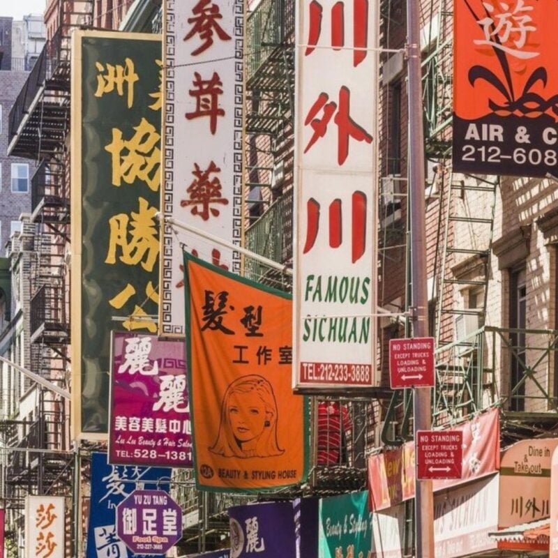 Colorful storefront signs in Chinese and English along a bustling street in New York City's Chinatown