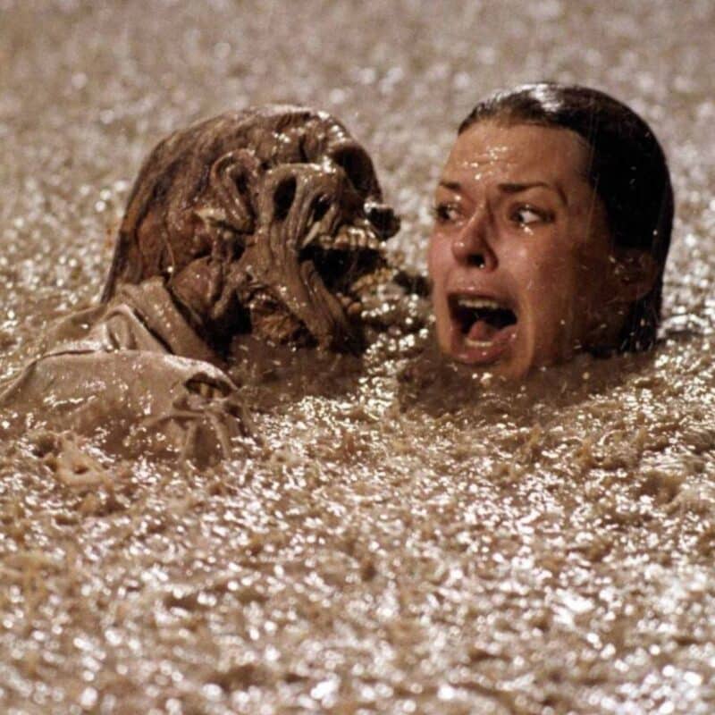 A woman with a frightened expression emerging from muddy water alongside a decayed skeleton