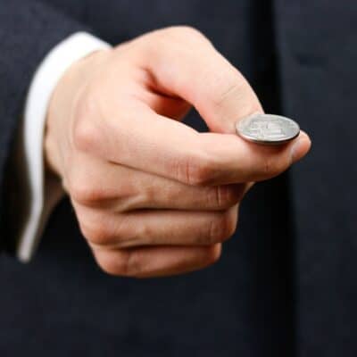 A person holding a coin between their fingers, poised for a coin toss