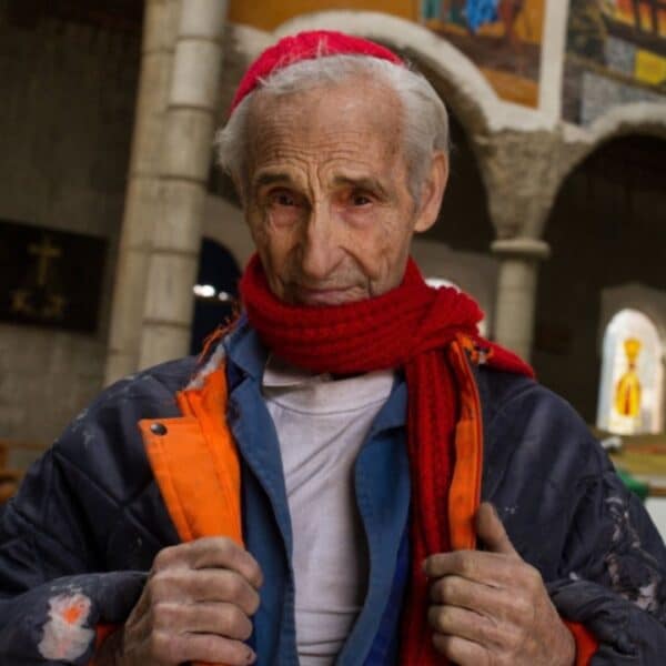 Justo Gallego Martínez, wearing a red scarf and hat over a blue jacket