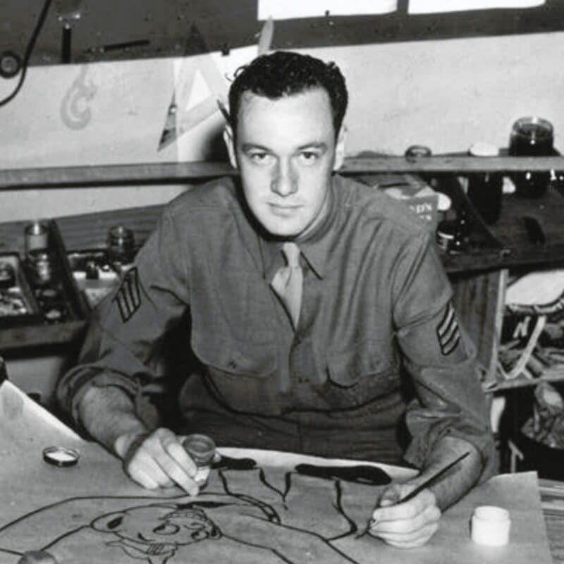 Stan Lee in a U.S. Army uniform drawing at a drafting table during World War II
