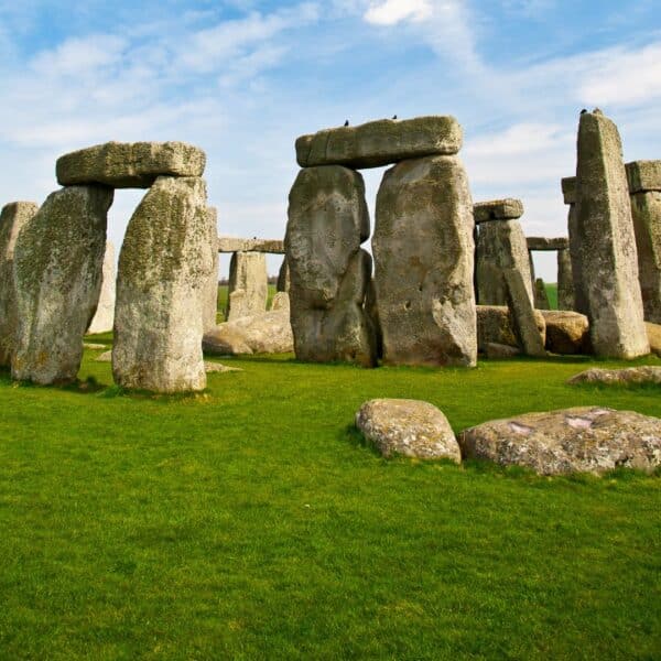 Stonehenge with several upright and horizontal stones on a grassy field under a blue sky