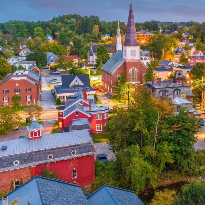 Colorful evening view of a historic town in Vermont, featuring a large brick church with a tall, patterned steeple