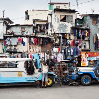 A densely packed area with worn buildings, colorful clothes hanging on lines and a man repairing a vehicle