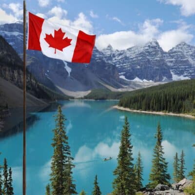 Canadian flag next to a serene lake with evergreen trees and snow-capped mountains