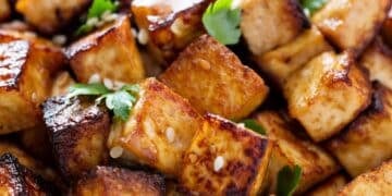 Close-up of golden-brown cooked tofu cubes garnished with fresh herbs and sesame seeds
