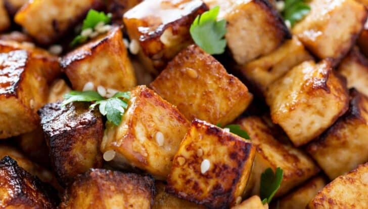 Close-up of golden-brown cooked tofu cubes garnished with fresh herbs and sesame seeds