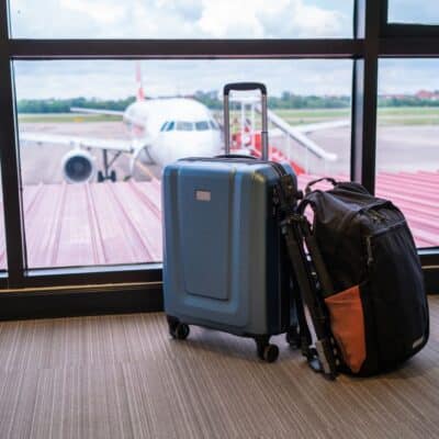 Luggage and a backpack sit by an airport window, with a plane visible on the tarmac